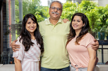Happy indian senior father standing with his two young daughters smiling looking at camera.