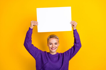 Photo of positive adorable lady wear trendy clothes arms up hold paper empty space presenting...