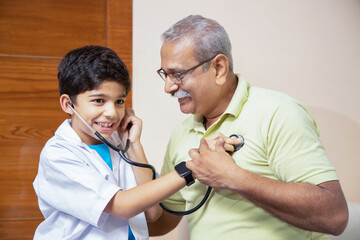 Playful indian boy kid wearing doctor uniform dress standing doing check heartbeat of with his...
