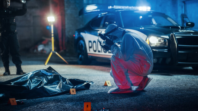 Crime Scene Investigation Team Working on a Case of Homicide at Night. Forensics Specialist Professionally Taking Pictures of the Dead Victim in a Body Bag. Potential Serial Killer on the Loose