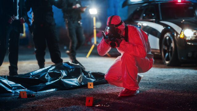 Forensics Specialist Taking Photos of Marked Evidence on a Crime Scene at Night. Expert Finds Glasses on the Floor, Potentially Belonging to the Dead Victim, and Professionally Takes Photos of it
