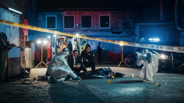 Team of First Responders Arriving at a Murder Scene in a Back Alley. Police Officer and Detective Making Preliminary Assumptions of the Potential Events of the Night and Consider the Evidence and Body