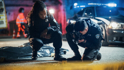 Female Black Inspector Supervising a Young Asian Man Who Newly Joined the Ranks of Police Departement in his First Crime Scene Task. Investigation Team Working on Murder Case During Night - obrazy, fototapety, plakaty