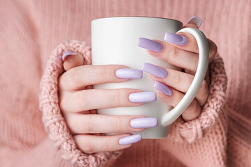 Girl's hands with delicate purple manicure holding a cup of tea.