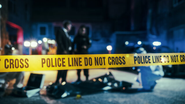 Close Up on Crime Scene Yellow Tape Showing Text "Police Line Do Not Cross". Restricted Area to the Public. Police on Duty in the Background. Cinematic Bokeh Effect With Red and Blue Neon Lights