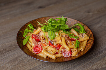 Close-up of palatable pasta with cherry tomatoes, arugula rucola and cheese served on brown round plate on wooden table.