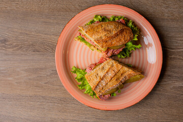 Top view of flavorous sandwich from crispy bread baguette, fresh lettuce and ham on pink plate on brown wooden table.