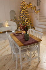 Christmas or New year decoration on white modern kitchen at cozy apartment. Long festive table with chairs in the middle. Beautiful stylish room.