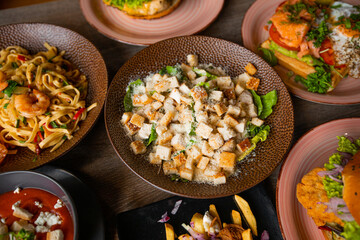 Top view of toothsome food on plates on wooden table in restaurant cafe. Pasta with shrimps. Caesar salad with lettuce.