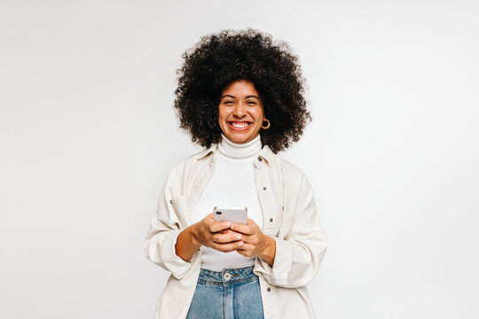 Cheerful young woman smiling at the camera while holding a smartphone