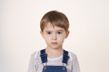 A serious little blond boy looks skeptical on a white background. the kid raised one eyebrow