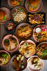 Top view of tasty food on table in restaurant. Pasta with shrimps. Caesar salad. Tomato soup. French fries. Burgers.