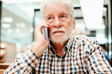 Portrait of a caucasian serious man using mobile phone - handsome bearded elderly man sitting thoughtfully while holding mobile phone