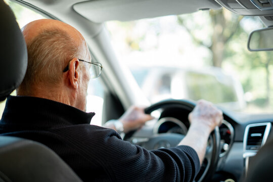 Back view of senior caucasian man with hands over the steering wheel driving his car