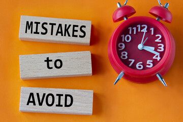 MISTAKES to AVOID - words on wooden blocks on orange background with red clock