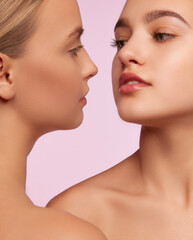 Beauty procedure face care. Portrait of two young, beautiful girls with well-kept skin isolated over pink studio background. Concept of skincare, cosmetology, natural beauty