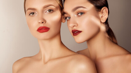Portrait of two young, beautiful girls with red lips makeup and perfect skin isolated over grey studio background. Shadows. Concept of skincare, cosmetology, natural beauty - obrazy, fototapety, plakaty