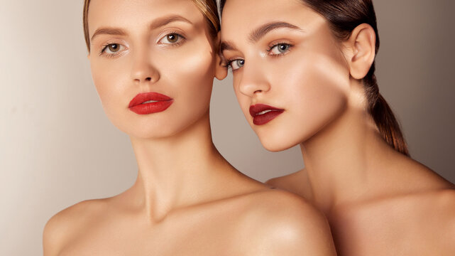Portrait of two young, beautiful girls with red lips makeup and perfect skin isolated over grey studio background. Shadows. Concept of skincare, cosmetology, natural beauty