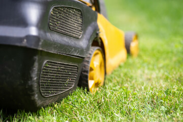 Lawn mower cutting green grass, spring, summer gardening background. Lawn care.