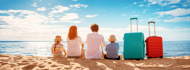 Mother and father with their children sitting on the beach with suitcases.