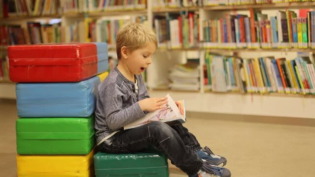 Adorable little child, boy, sitting in library, reading book and choosing what to lend, kid in book store