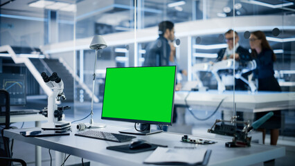 Fototapeta premium Industrial Research Laboratory with Desktop Computer with Green Screen Mock Up Display. Scientific Lab, Engineering Research Center with Specialists Working on Robot Development in the Background.
