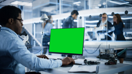 Naklejka premium Software Developer Working on Computer with Green Screen Mock Up Display. Scientific Lab, Engineering Research Center with Specialists Working on Mobile Robot Development in the Background.