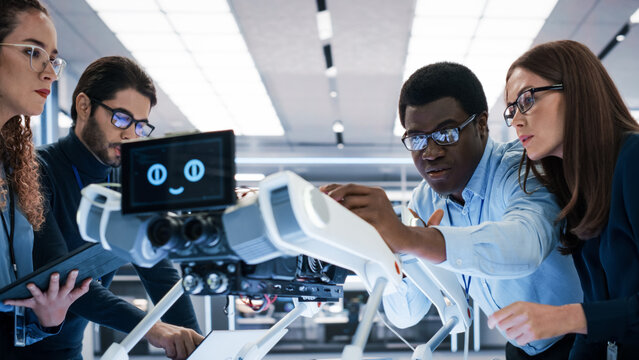 Professional International Team of Female and Male Engineers Use Industrial Programmable Robot Dog in a Factory Development Workshop. Tech Facility with Machines, Computers and Research Equipment.