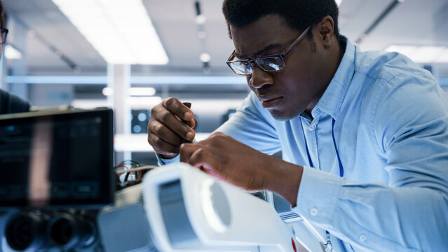 Close Up Portrait of an African American Robotics Engineer Setting Up a Robot Dog Prototype, Using a Screwdriver to Fasten the Bolts. Scientist Connect a Motherboard to a Mobile AI Four-Legged Robot.