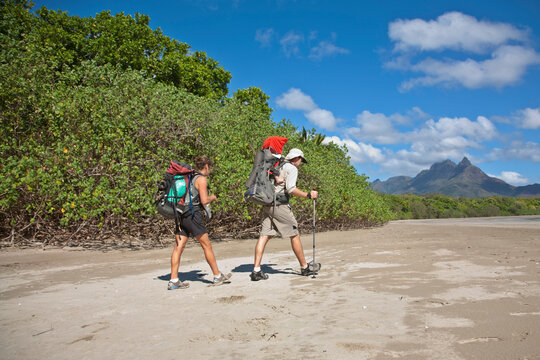 A man and woman with their baby hike along Zoe Bay, Hinchinbrook Island, Queensland, Australia.