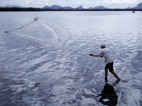 Man throwing and pulling in fishing net in river, Vitoria, Espirito Santo, Brazil.