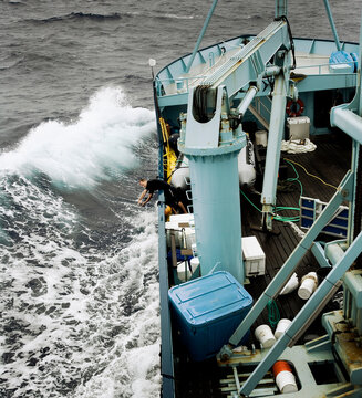crew member hanging off the side of boat as wave hits