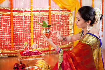 Young pretty woman making saathiya swastik symbol on kalash with roli for puja. A woman wearing...