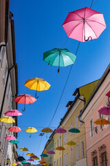 Fototapeta na wymiar Viele bunte Regenschirme hängen zwischen den Häusern vor einem blauen Himmel