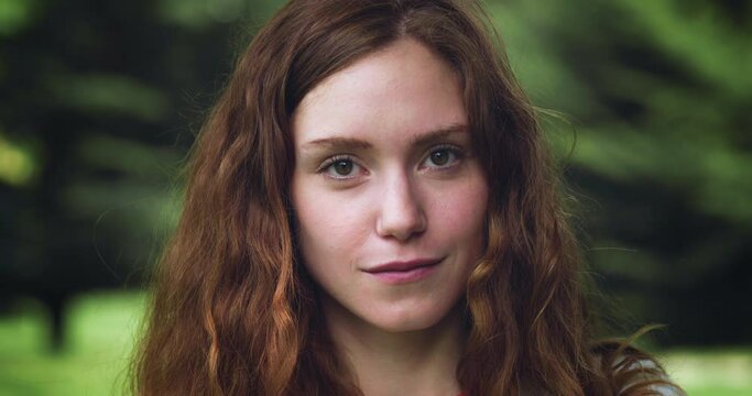 Close up Portrait of a Young Redhead Woman Looking at the Camera in a Green Park During Evening Time. Pretty Teenager with Auburn Hair Enjoying Fresh Air in the Park and Taking Care of her Wellbeing