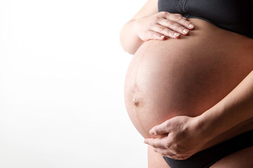 A pregnant girl in black underwear, holding her stomach with her hands. On a white background, banner, copy space.