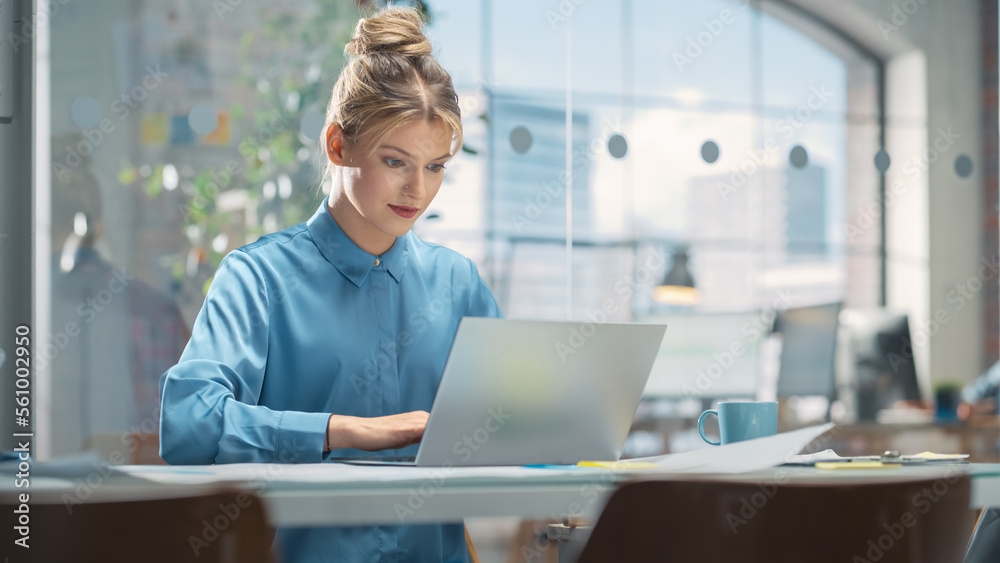 Poster portrait of white creative young woman working on a laptop computer in bright office. female team le