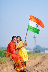 Indian rural woman and her little daughter waving national tricolor flag at agriculture field.