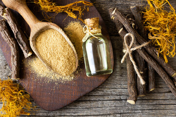 Glass bottle of licorice root essential oil with liquorice fiber on rustic background ( glycyrrhiza glabra )