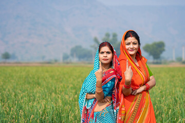 Indian rural women smiling and showing voting sign at agriculture field.