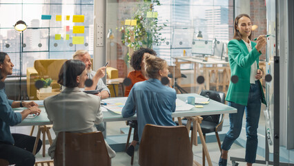 A Young Caucasian Woman Presenting Statistics on Funding Using Charts and Whiteboard. A Female Analyst Discussing Data in Office Meeting with Multiethnic Diverse Group