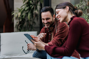 Smiling people, searching something online while sitting next to each other, at the office.
