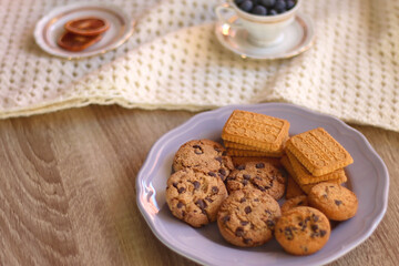Plate of cookies, cup of tea, fresh blueberries, dry oranges, stack of books, reading glasses and tablet on the table. Hygge at home. Selective focus.