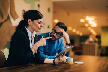Focused male and female employees discussing work, looking at the tablet, and sitting at the office.