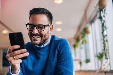 Male boss reading a text message on mobile phone and smiling.