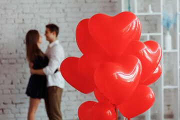 Air balloons in shape of heart with the couple in love on background.Hugging, kissing and enjoying spending time together while celebrating Saint Valentine's Day.