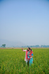 Indian farmer with wife spreading hand and giving expression at field.