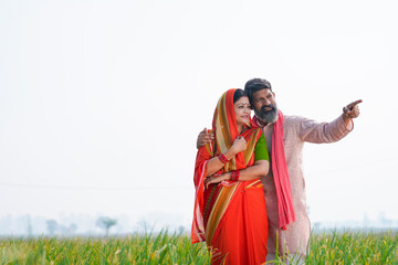 Indian farmer with wife spreading hand and giving expression at field.