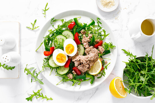 Salad with canned tuna, boiled egg, arugula and fresh vegetables. Top view