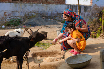 Indian rural woman with daughter feeding black buffalo. - Powered by Adobe